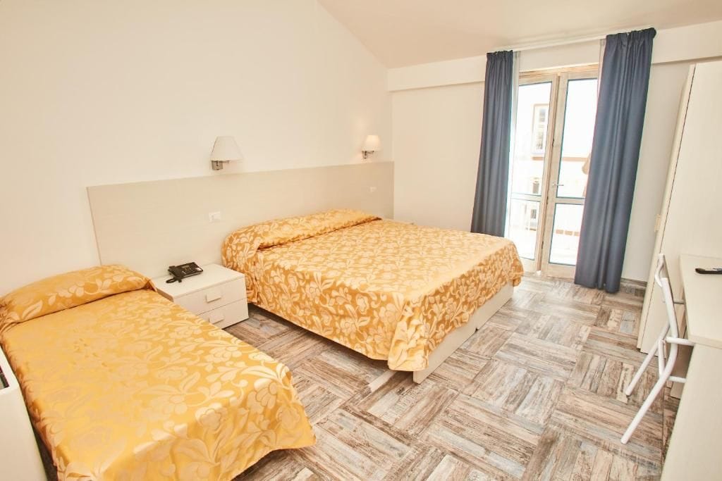 Habitación de hotel con dos camas, un escritorio y una ventana con cortinas.