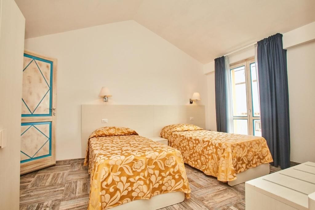 A room with two beds, a door with geometric design, and a window with curtains.