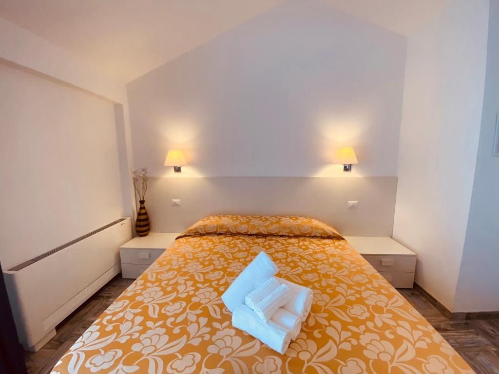 A hotel room with a bed, bedside lamps, a vase, and a folded towel.