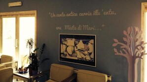 A room with a dark blue wall, a framed quote, a framed artwork, a plant, and a wooden chair. - Hotel Mûita di Mari (Santa Teresa di Gallura)