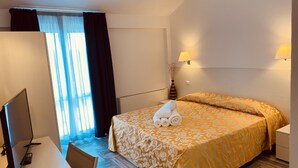 A hotel room with a bed, a desk with a computer, and a window with curtains. - Hotel Mûita di Mari (Santa Teresa di Gallura)