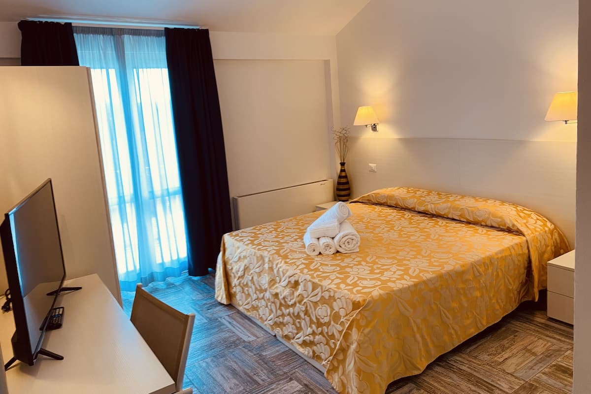 Una habitación de hotel con cama, escritorio con computadora y ventana con cortinas.
