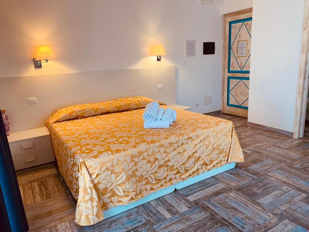 A hotel room with a bed, two wall-mounted lamps, a wooden door with a geometric pattern, and a tiled floor.
