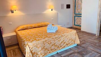 A hotel room with a bed, two wall-mounted lamps, a wooden door with a geometric pattern, and a tiled floor.