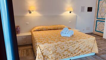 A neatly made bed with a floral bedspread, two wall-mounted lamps, a vase on the nightstand, and a wooden door with geometric patterns.