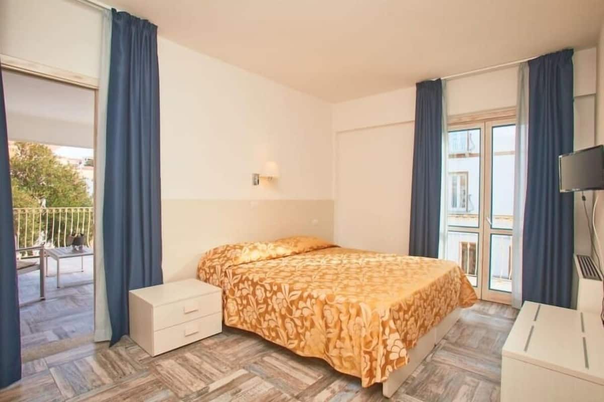 Un dormitorio con cama, mesita de noche, cómoda y ventana con cortinas.