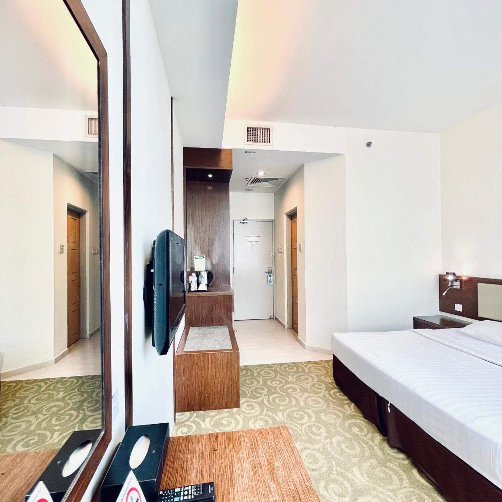 A hotel room with a bed, a desk, a television, and a mirror.