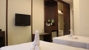 A hotel room with two beds, a flat-screen TV, a mirror, and a small desk with a kettle and water bottles.