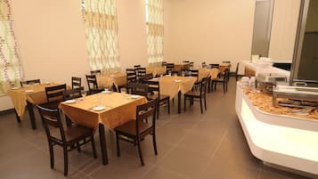 A dining area with multiple tables and chairs, a buffet station, and decorative curtains.