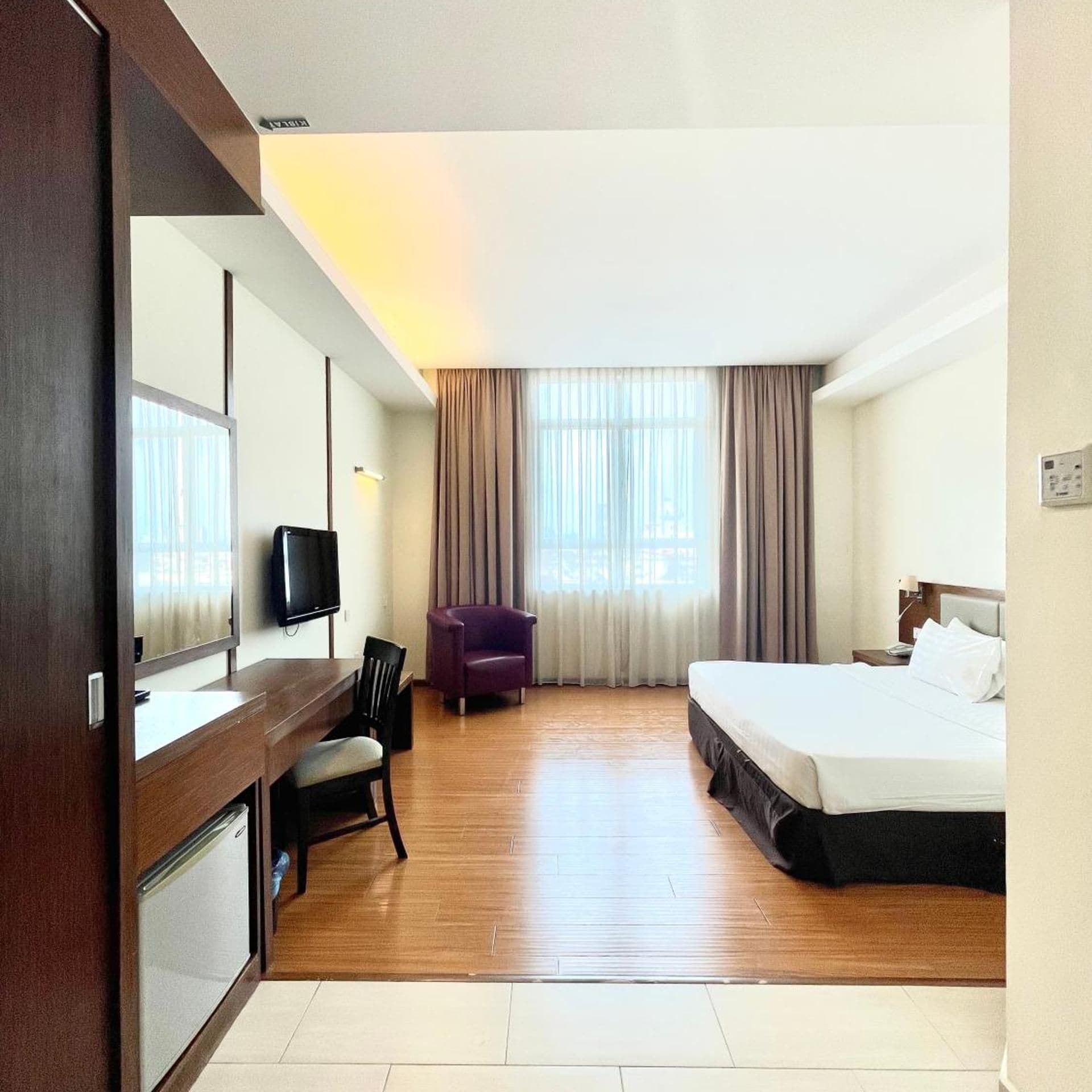 Une chambre d’hôtel avec un lit, un bureau et une chaise, une télévision et une fenêtre avec des rideaux.