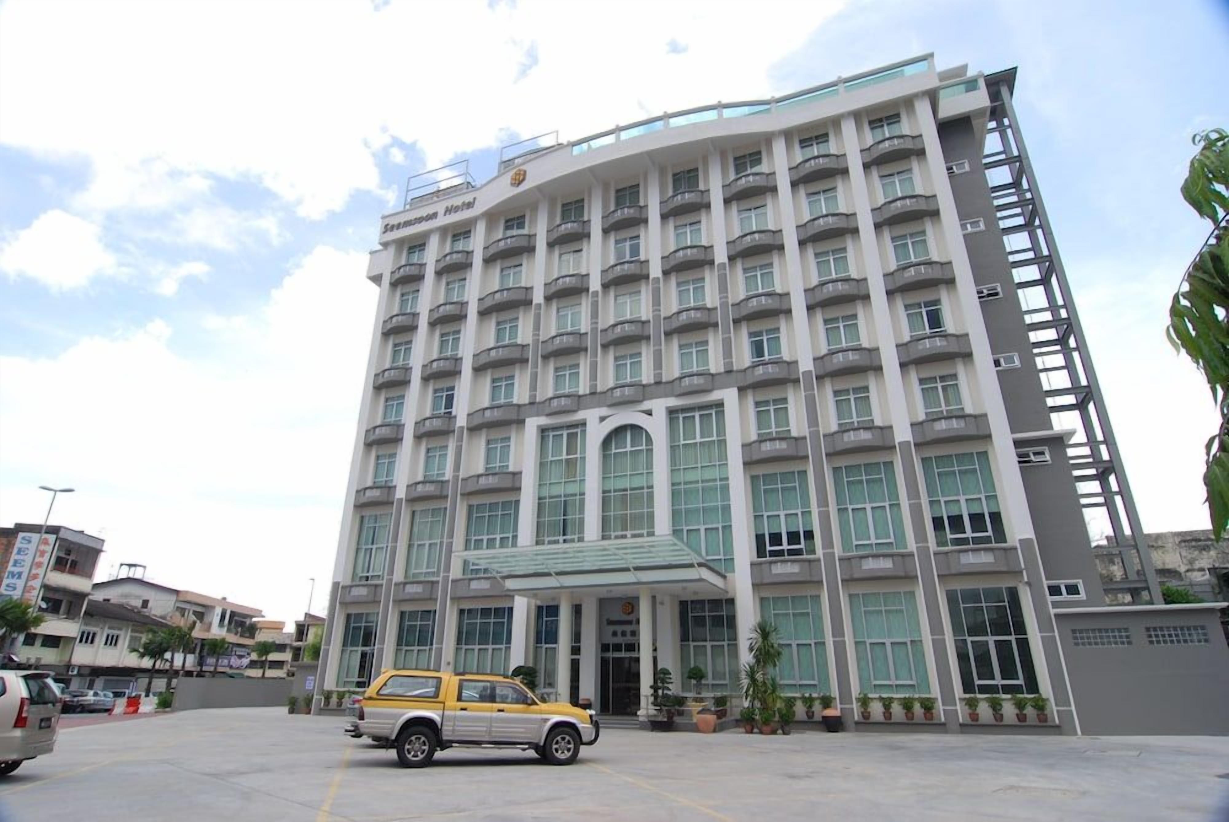 A multi-story hotel with a modern design, featuring a prominent entrance and a parking area in front.