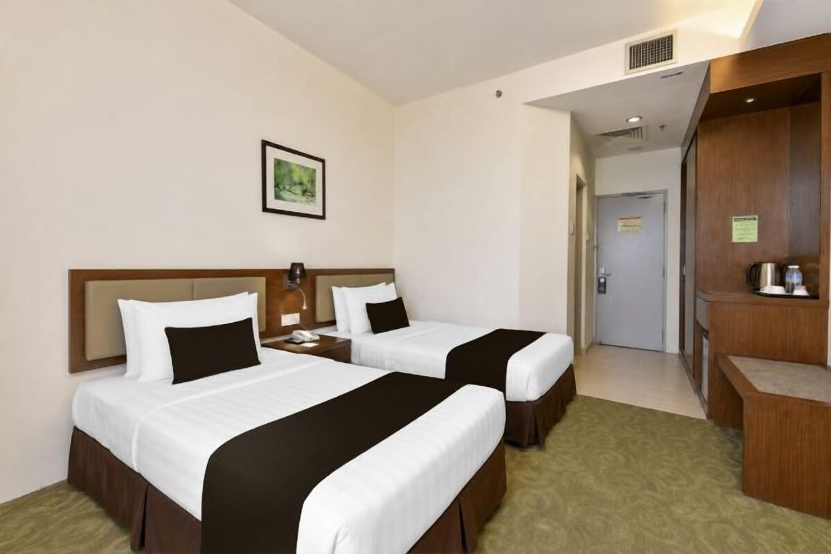Une chambre d’hôtel avec deux lits, une table de chevet, un bureau, une chaise et un petit coin cuisine.