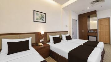 A hotel room with three beds, a bedside table with a lamp, a telephone, and a framed picture on the wall.