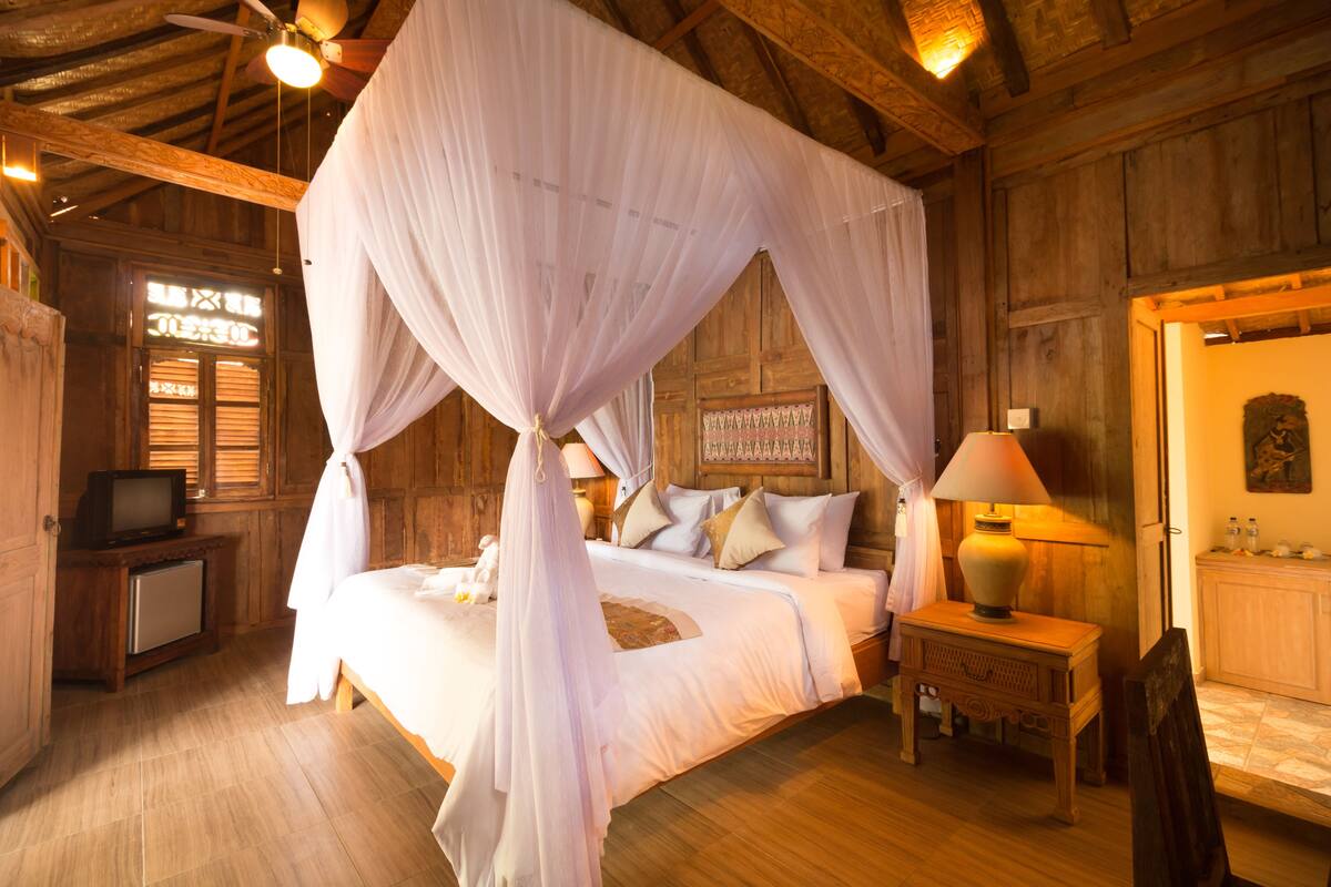 A wooden room with a bed under a canopy, a television on a small table, and a lamp on a nightstand.