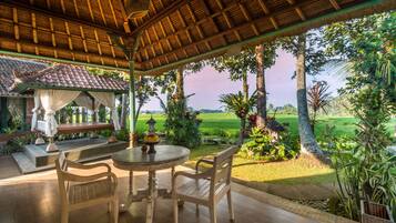 Un espacio al aire libre cubierto con una mesa y sillas, rodeado de exuberante vegetación y vistas a un campo verde.