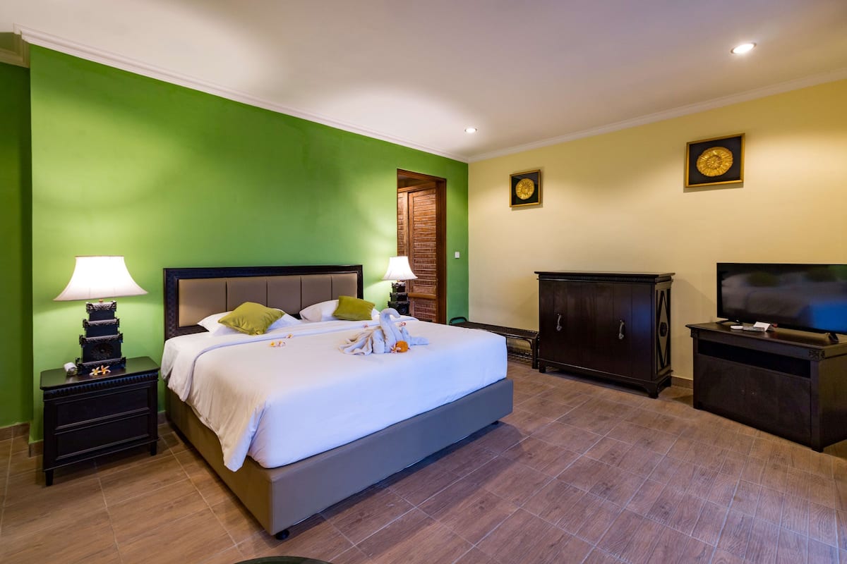 A hotel room with a large bed, two bedside tables, a TV, a wardrobe, and a green wall.
