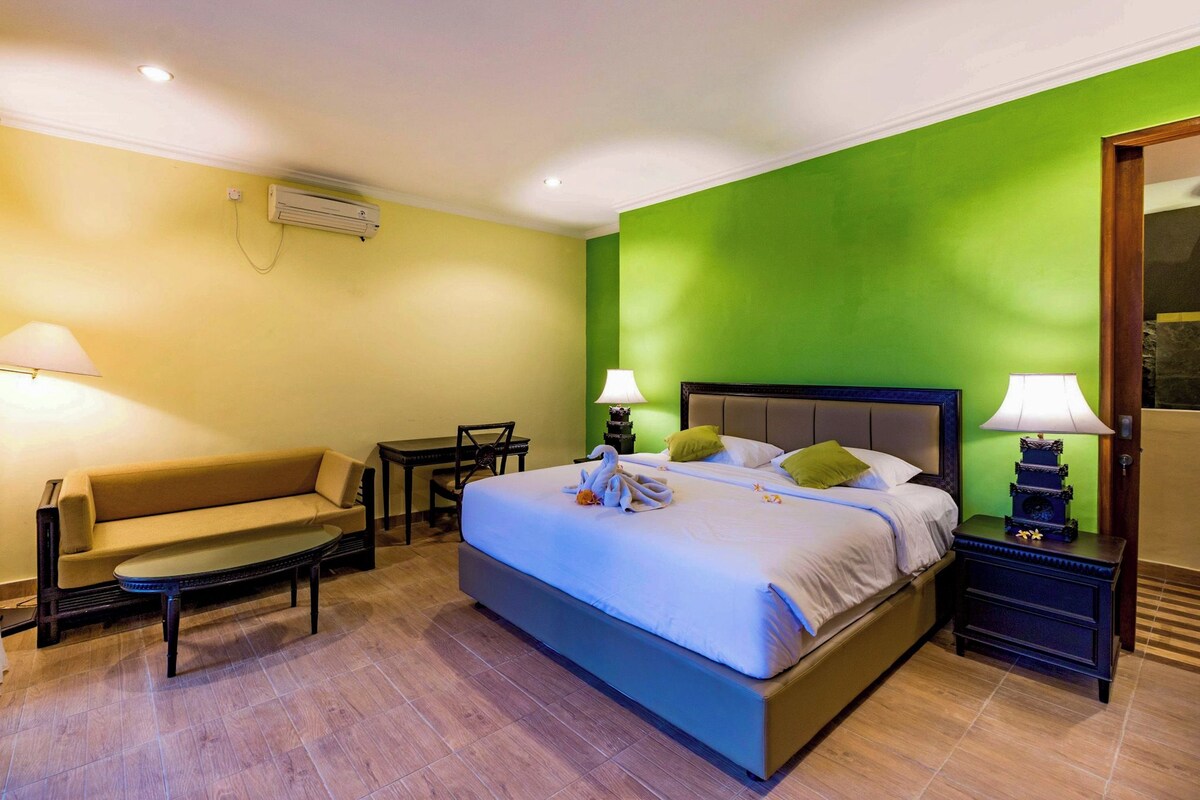 Habitación de hotel con cama, sofá, una mesita, dos lámparas y un equipo de aire acondicionado.
