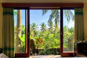 A room with a large sliding glass door leading to a tropical garden view.