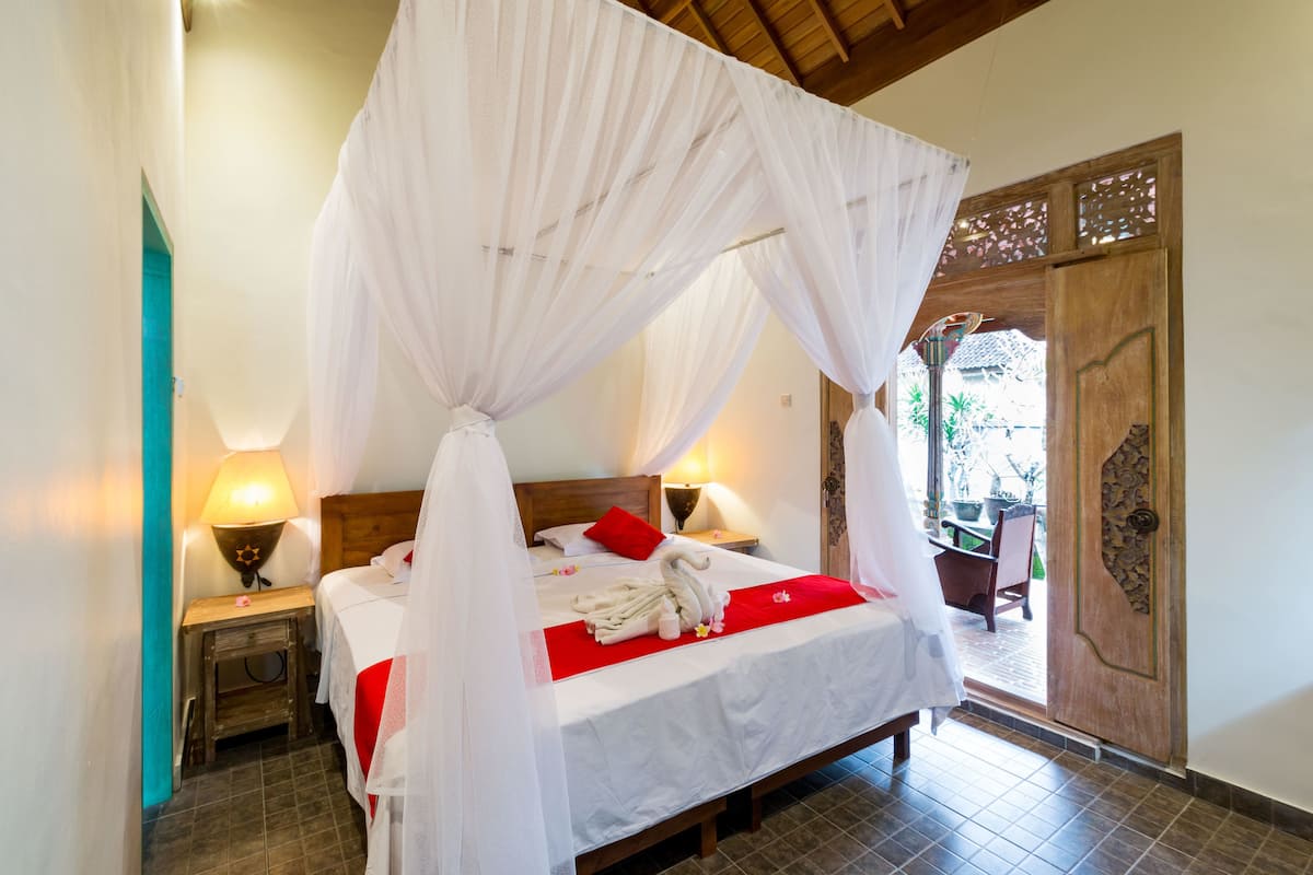 A bed with a canopy, two bedside lamps, a red pillow, and a wooden door.