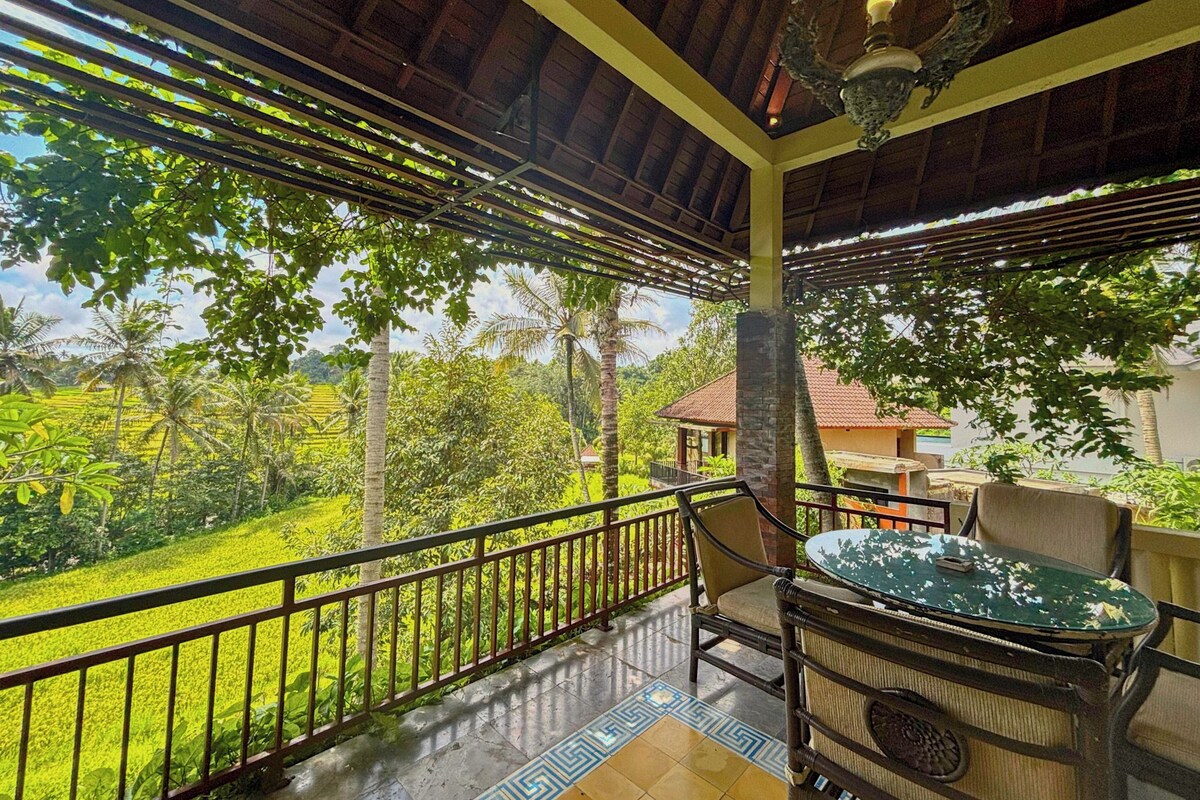 Un balcón con vistas a un paisaje verde exuberante, una mesa con sillas y un techo decorativo.