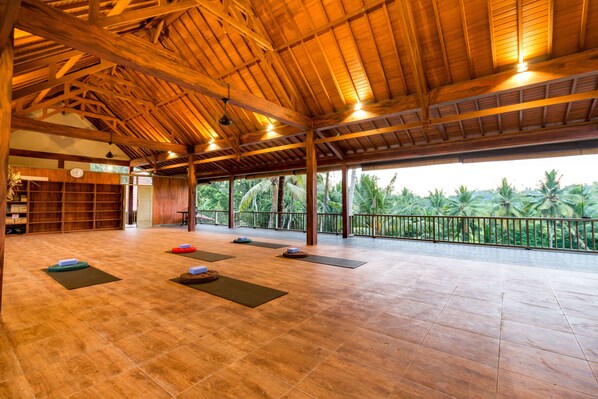 Amplio espacio interior con techo alto, vigas de madera y grandes ventanales con vistas a palmeras.