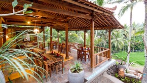 A wooden pavilion with a tiled floor, surrounded by tables and chairs, set against a lush garden backdrop. - Umasari Rice Terrace Villa (Mengwi)