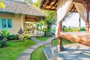 Un complexe hôtelier tropical doté d’une structure à toit de chaume, d’un espace de détente extérieur couvert et d’un sentier menant à une terrasse en bois.
