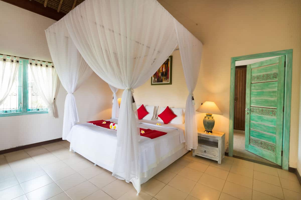 A room with a four-poster bed, a nightstand, a lamp, and a green door.