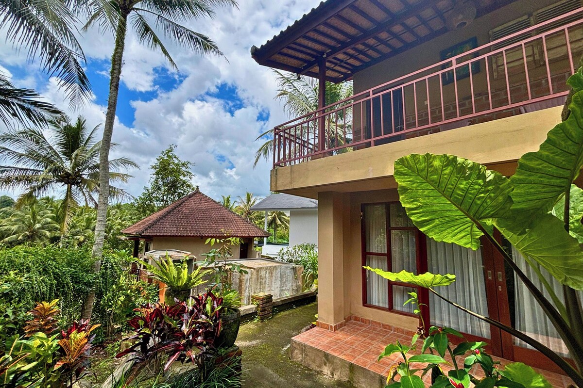 Un edificio de dos pisos con balcón, rodeado de exuberante vegetación tropical.