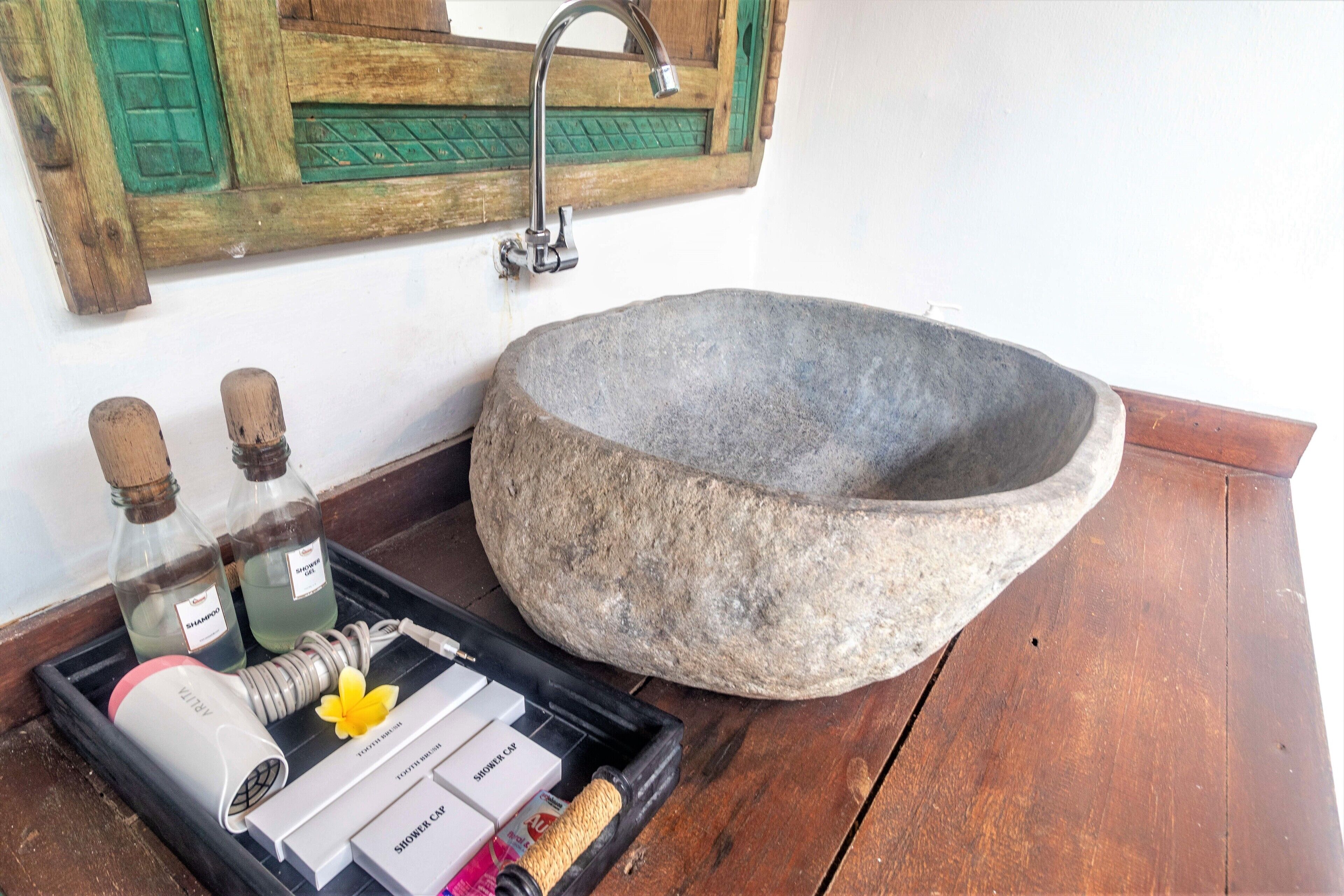 Un évier en pierre, avec un plateau en bois contenant des articles de toilette et un porte-savon pour la douche.