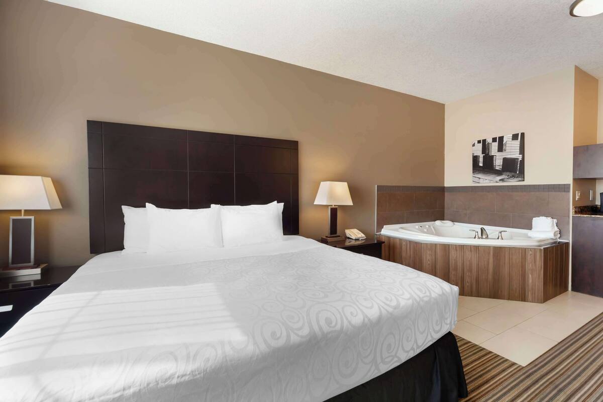 Ein Hotelzimmer mit einem großen Bett, einem Holzkopfstück, einer integrierten Badewanne und einer kleinen Küchenzeile.