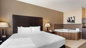 Una habitación de hotel con una cama grande, cabecera de madera, bañera integrada y una pequeña kitchenette.