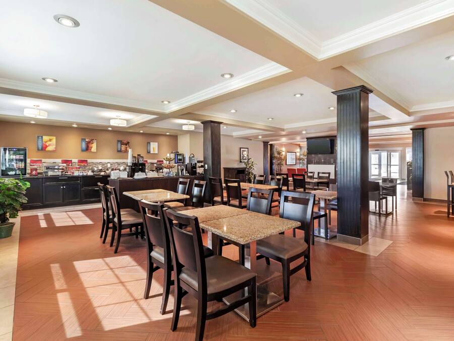 A spacious hotel lobby with multiple seating areas, a kitchen in the background, and a large television screen.