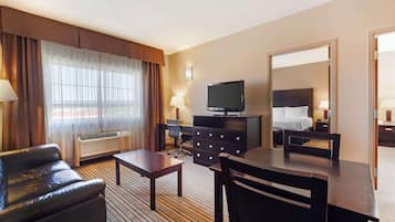 Una habitación de hotel con sofá de cuero, escritorio, televisor, cómoda y cama con cabecera.
