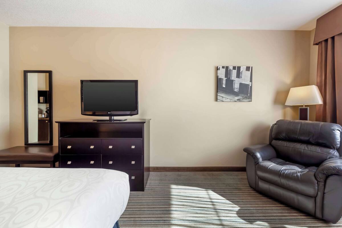 Ein Hotelzimmer mit einem Bett, einem Fernseher auf einer Kommode, einem Ledersessel, einer Lampe und einem Bild an der Wand.