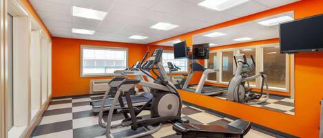 Un gimnasio con equipo de ejercicio, un espejo grande y un televisor en la pared.