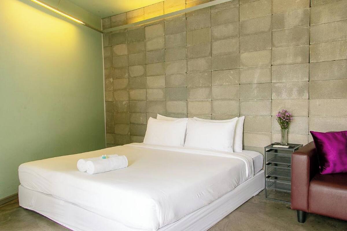 A hotel room with a large bed, a nightstand with a vase of flowers, and a leather sofa.