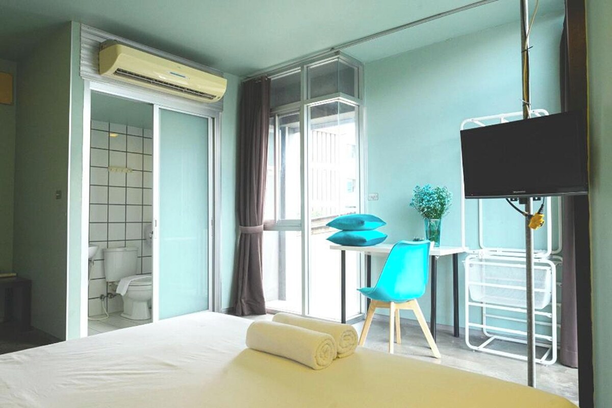 A hotel room with a bed, a desk with a chair, a TV, and a window with curtains.