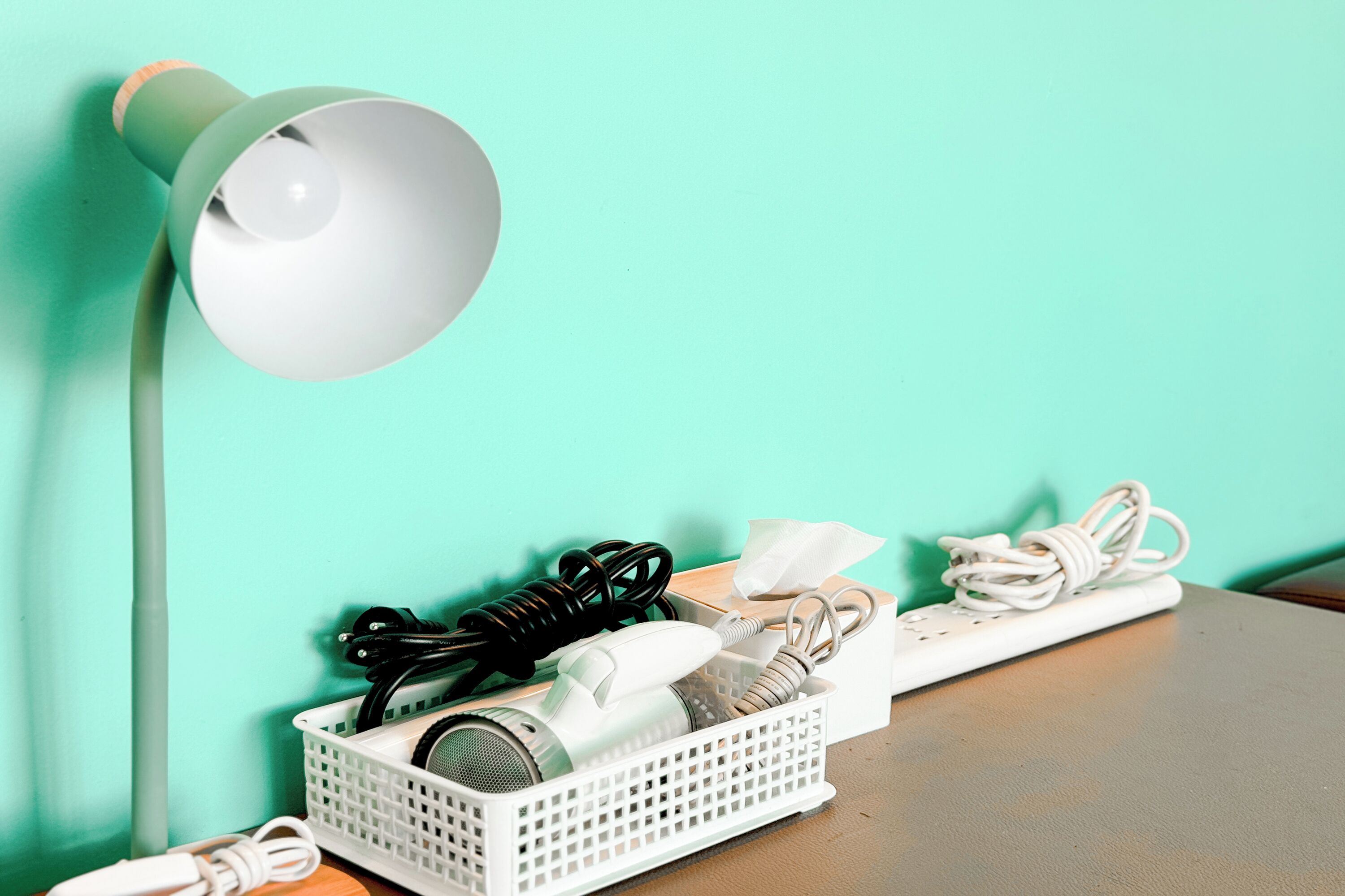 Un escritorio con una lámpara blanca, una regleta eléctrica blanca y una estación de carga blanca con cables.