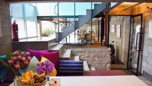 A modern interior with a staircase, a dining area with colorful cushions, and a table with a fruit bowl. - HeyHa House ChiangMai (Chiang Mai)