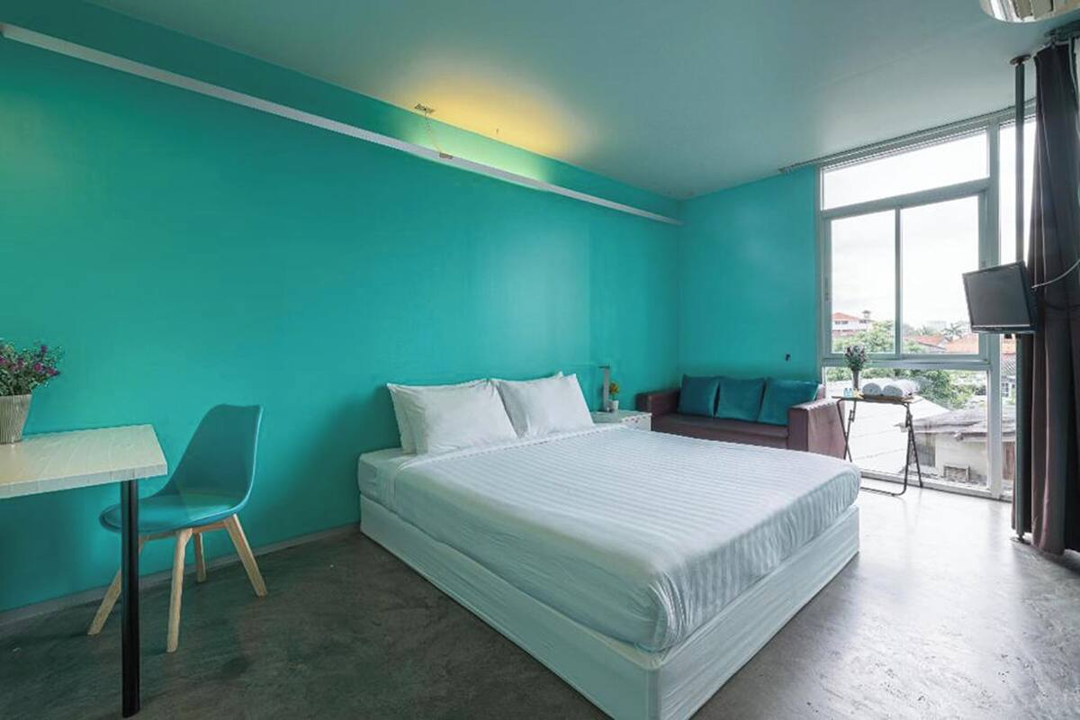 A bedroom with a bed, a desk, a chair, and a sofa.