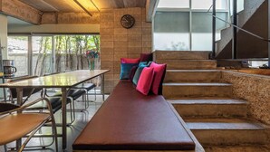 A modern kitchen with a long counter, a bench with colorful cushions, and a staircase. - HeyHa House ChiangMai (Chiang Mai)