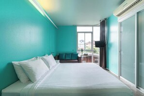 A bedroom with teal walls, a bed with white linens, a small seating area, and a window with a view. - HeyHa House ChiangMai (Chiang Mai)