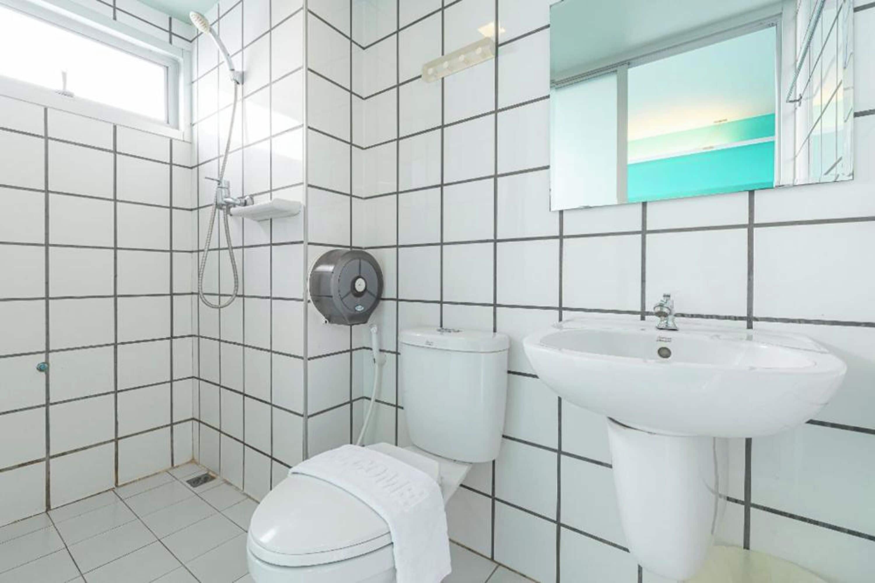Un baño con paredes de azulejos blancos, inodoro, lavamanos y ducha.