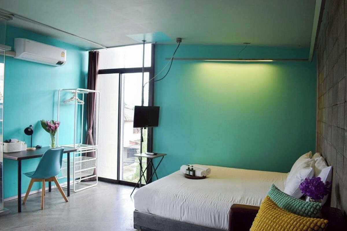 Una habitación de hotel moderna con una cama, un escritorio con una silla, un televisor y una ventana.