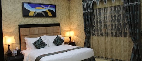 A hotel room with a large bed, two bedside lamps, a painting on the wall, and ornate curtains.
