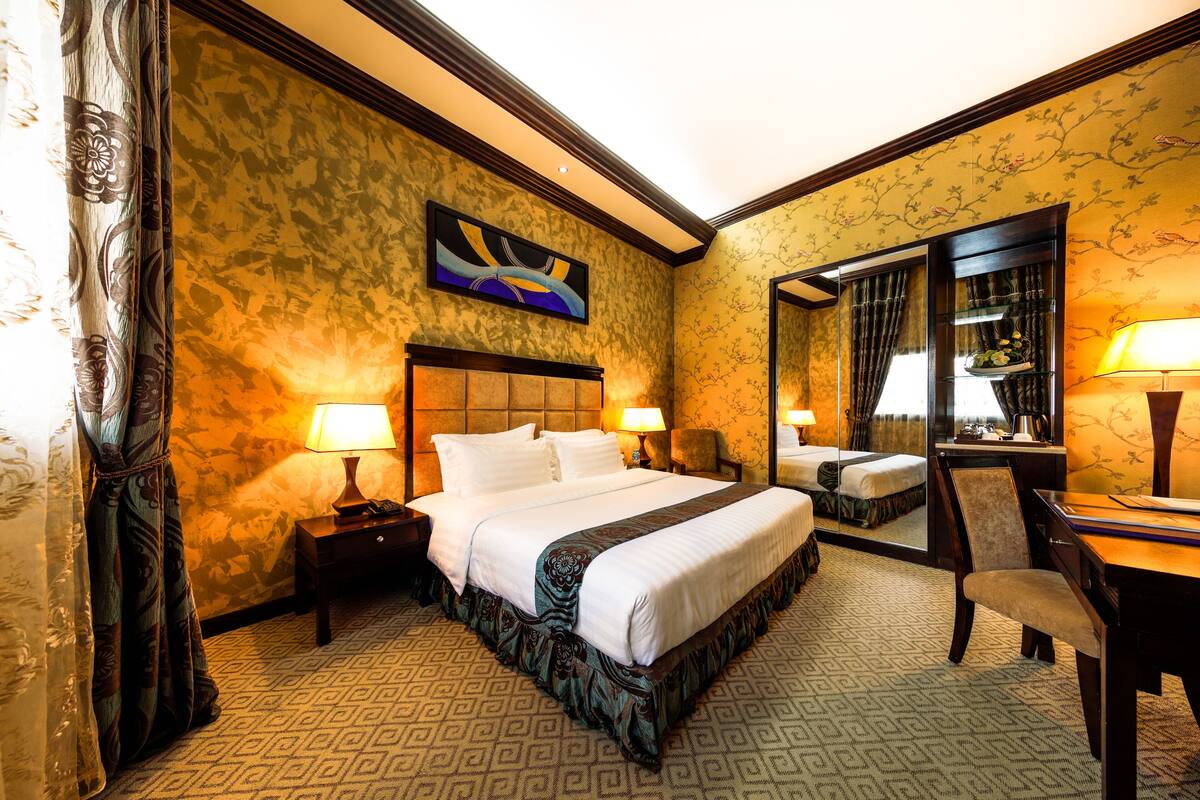 A hotel room with a large bed, two bedside tables with lamps, a chair, a desk, and a mirror.