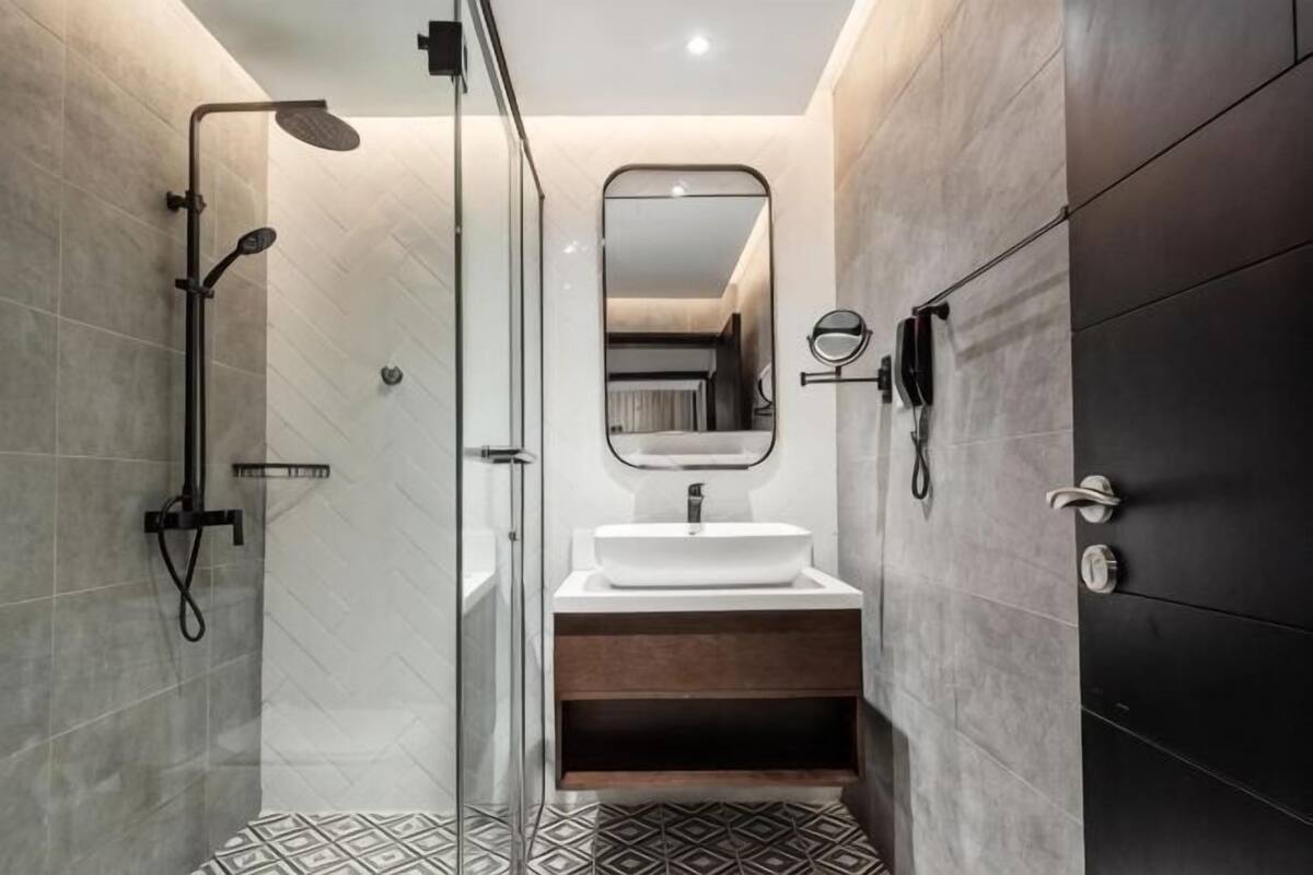 A modern bathroom with a glass shower enclosure, a white sink, and a dark tiled wall.