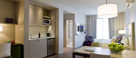 A modern hotel room with a kitchenette, a dining area, and a bed with a view.