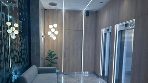 A modern lobby with a sofa, a potted plant, and two elevators.